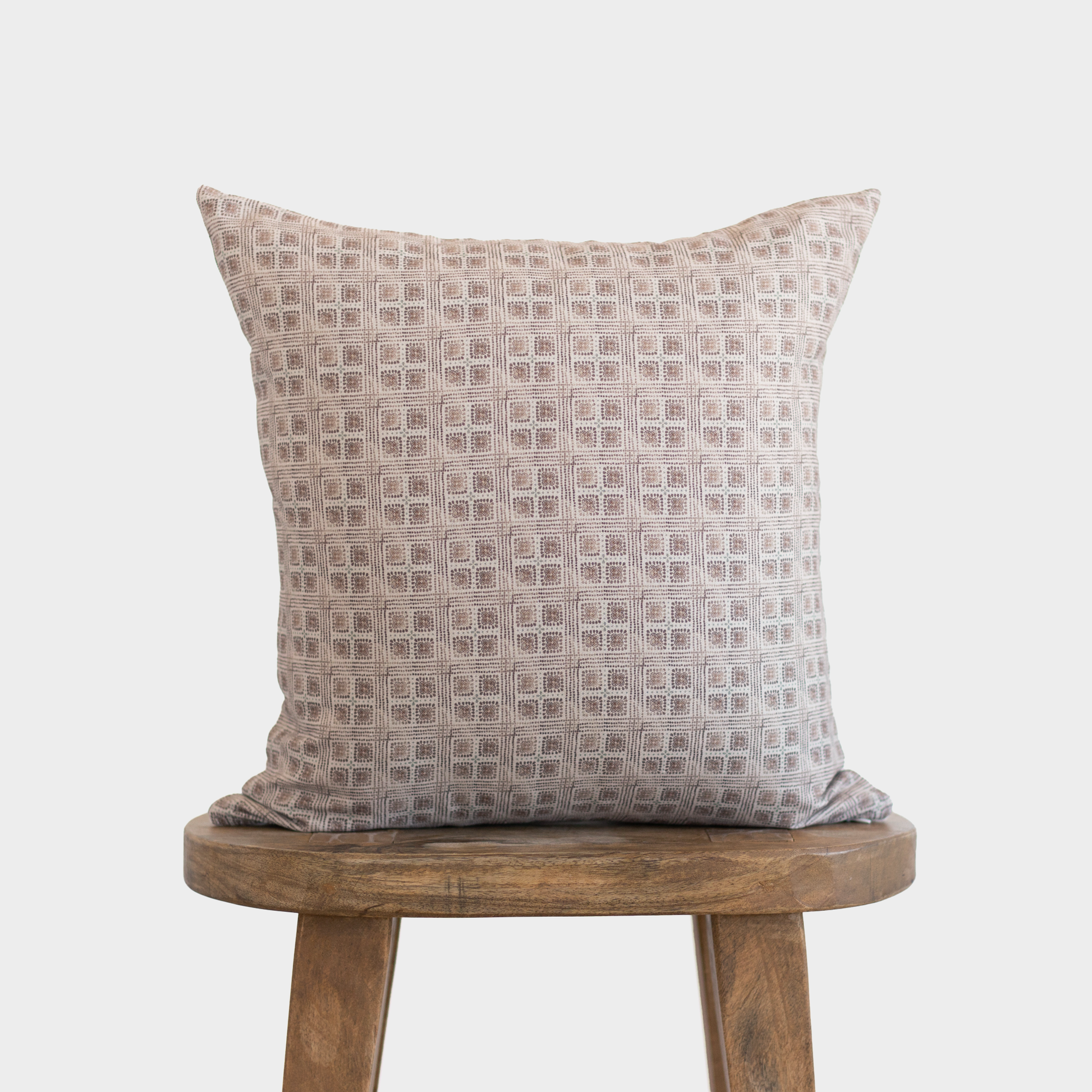 Brown and cream geometric grid patterned pillow with woven texture displayed on wooden stool.