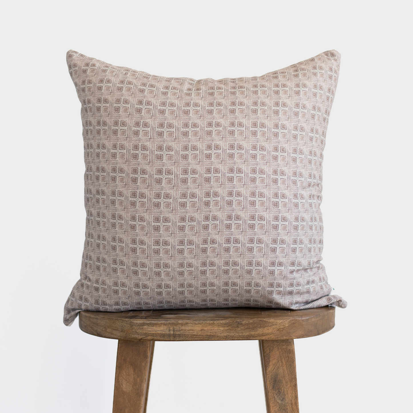 Brown and cream grid patterned square pillow displayed on wooden stool.