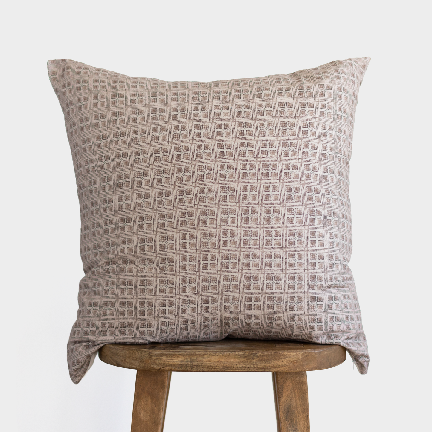 Brown and cream geometric grid patterned Euro pillow displayed on a wooden stool.