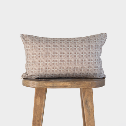 Brown lumbar pillow with geometric grid pattern displayed on wooden stool.