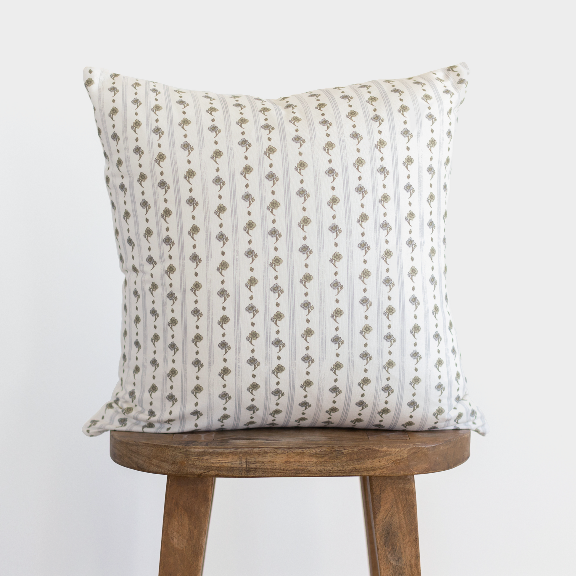 Cream pillow with vertical tan and gray striped pattern featuring geometric motifs, displayed on wooden stool.