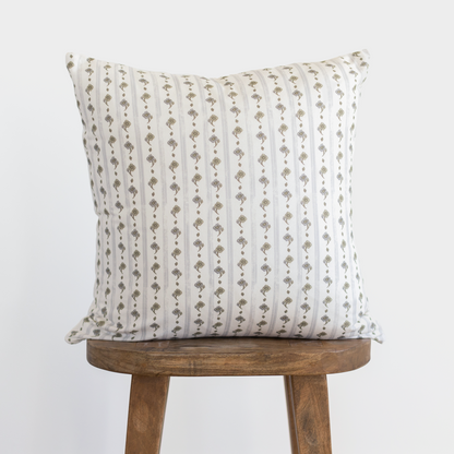 Cream pillow with vertical tan and gray striped pattern featuring geometric motifs, displayed on wooden stool.