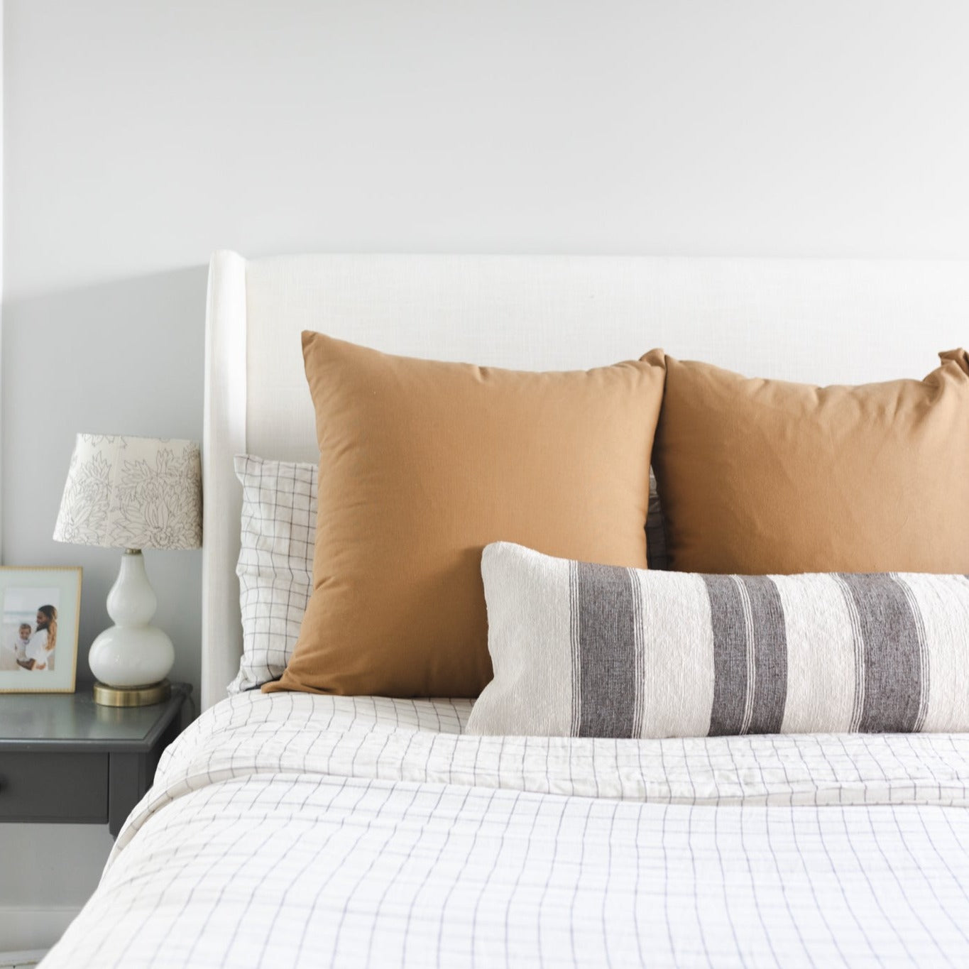Terracotta-colored throw pillow displayed on a bed with striped bedding and gray accent pillow.