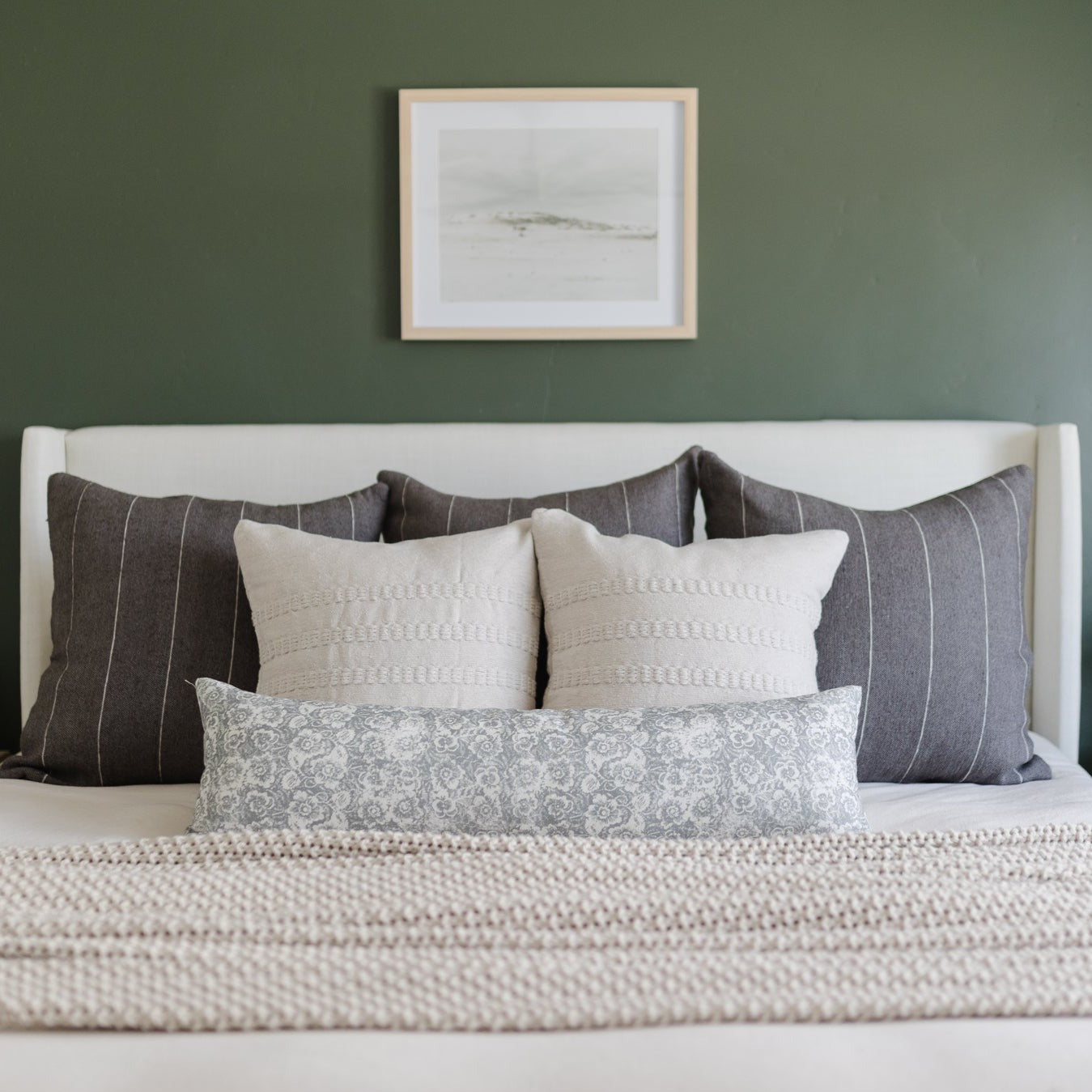 Gray lumbar pillow with floral pattern displayed on bed with coordinating decorative pillows.