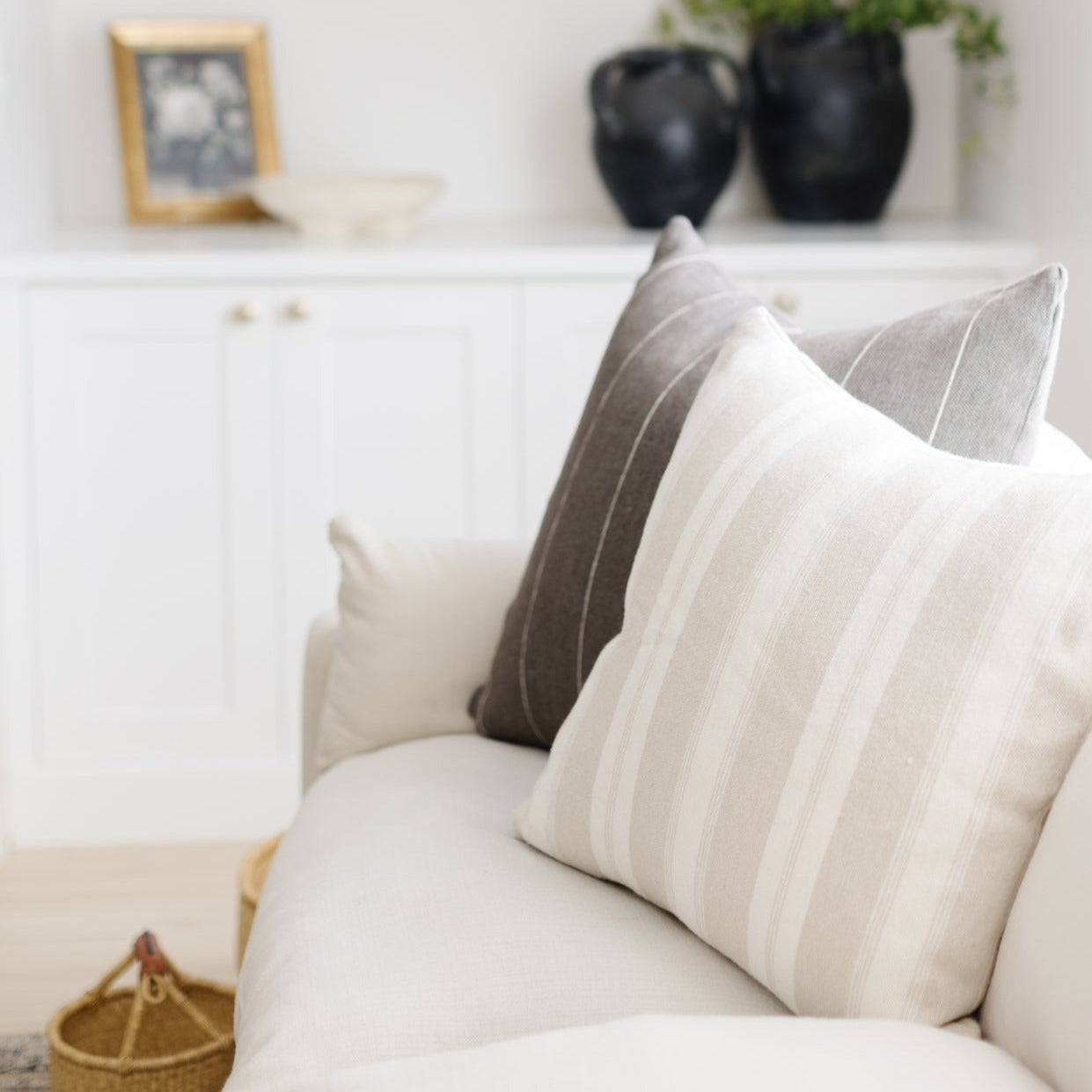 Tan striped throw pillow with vertical stripes displayed on a cream-colored sofa with matching pillows.