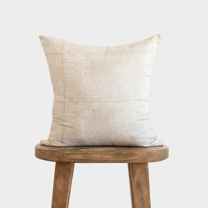 Cream pillow with faded floral pattern displayed on wooden stool.
