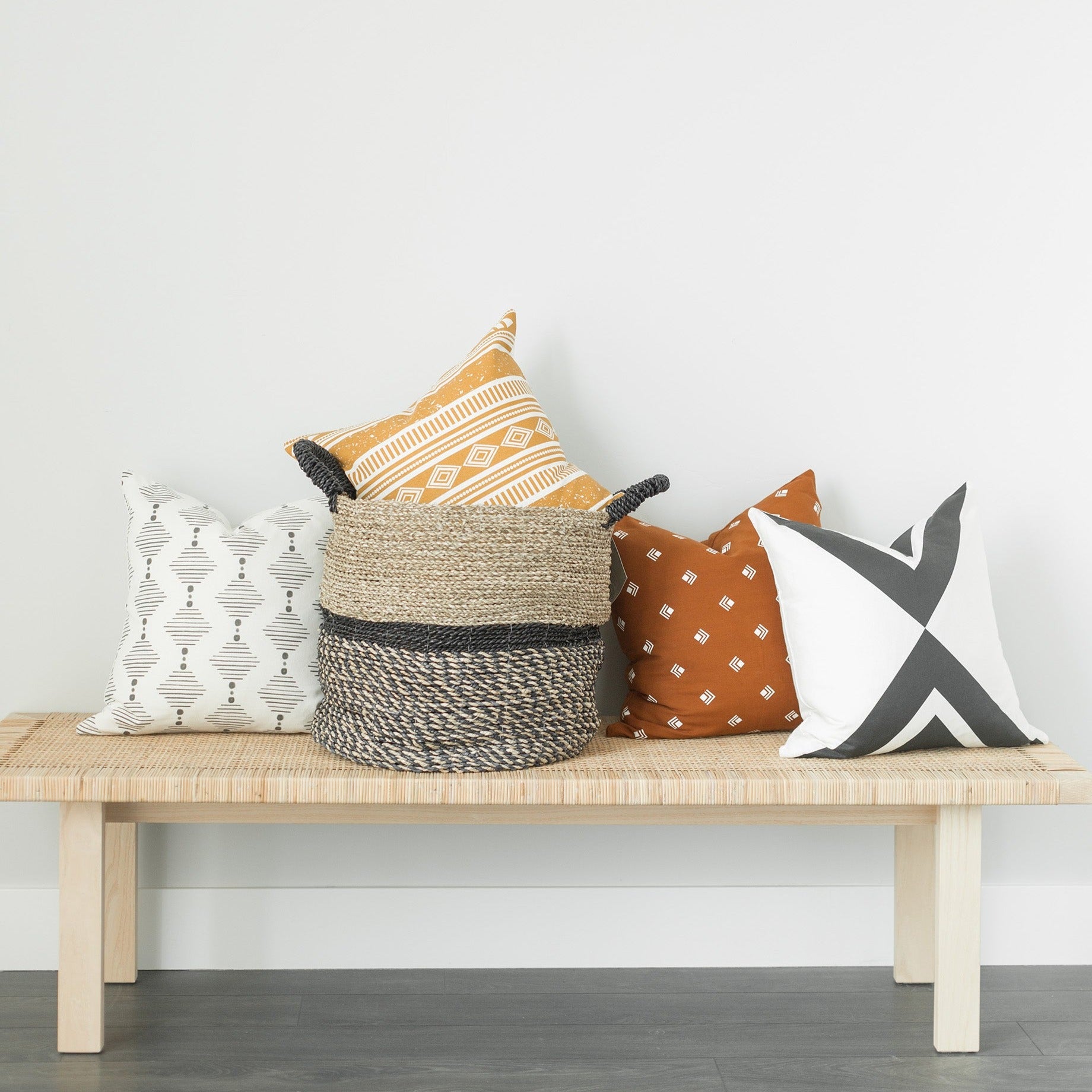 Four 18-inch decorative pillows in geometric and patterned designs displayed on a wooden bench.