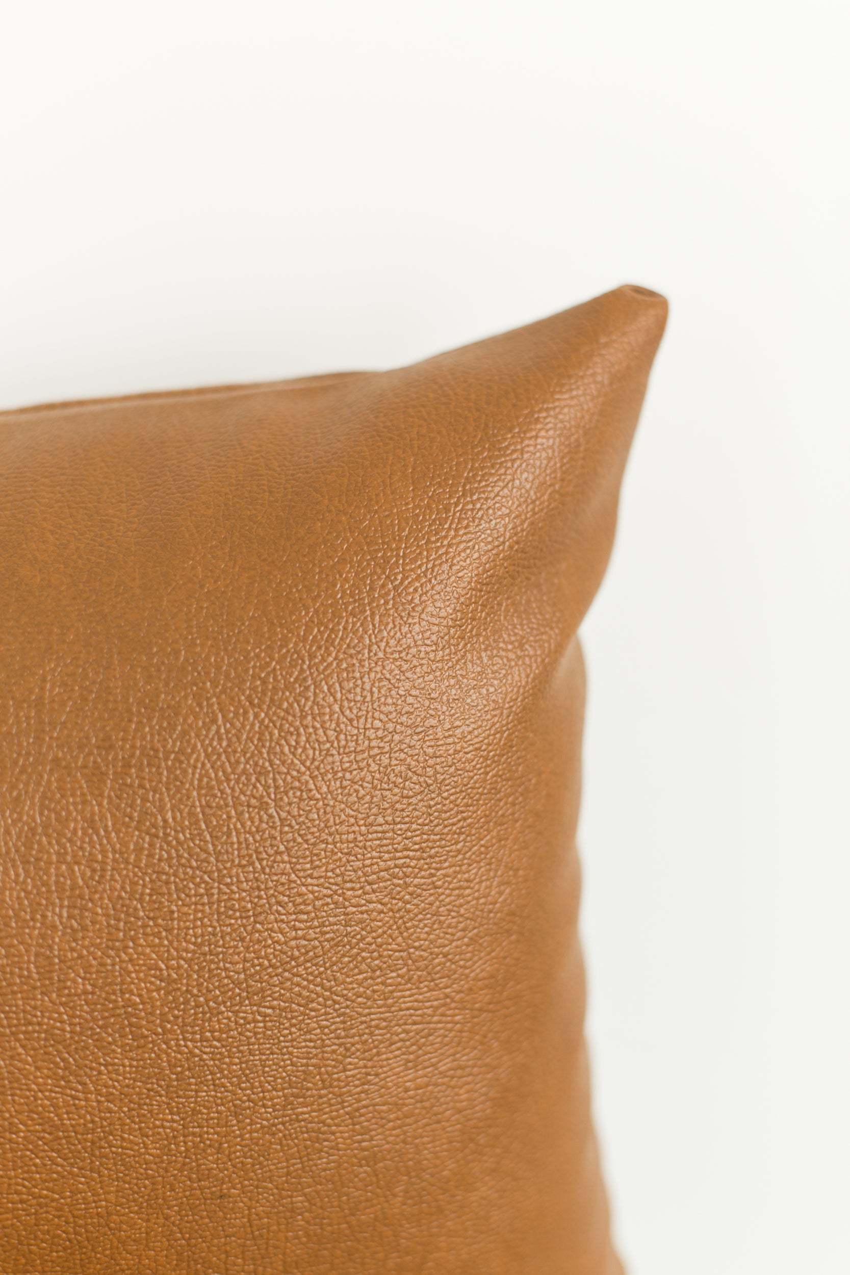 Tan leather lumbar pillow with textured surface and rounded corner detail.