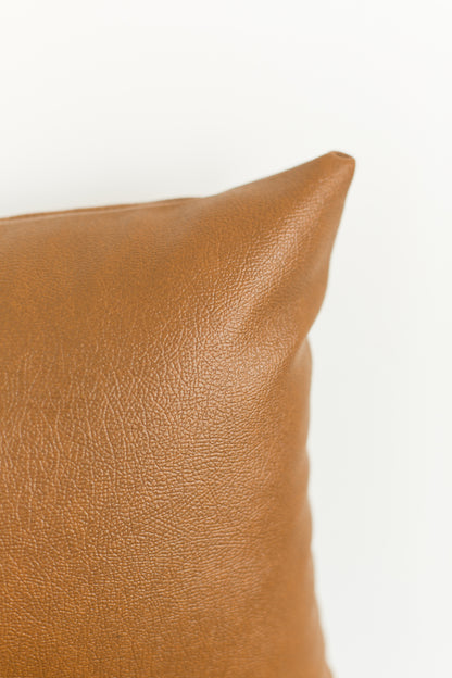 Tan leather lumbar pillow with textured surface and rounded corner detail.