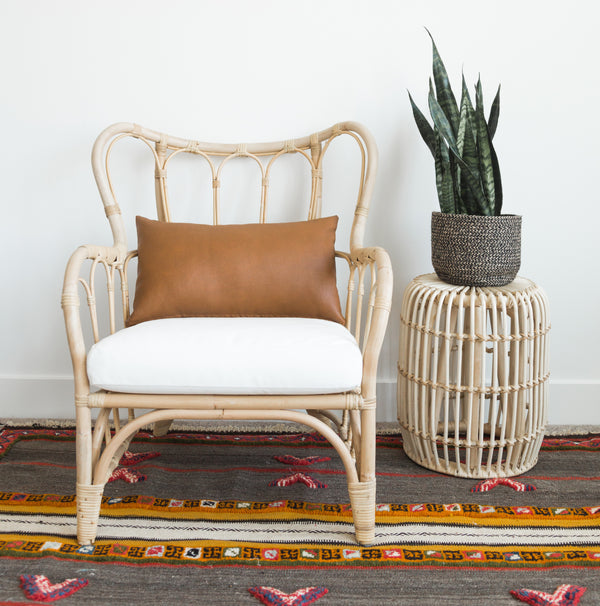 Tan leather lumbar pillow on natural rattan chair with white seat cushion.