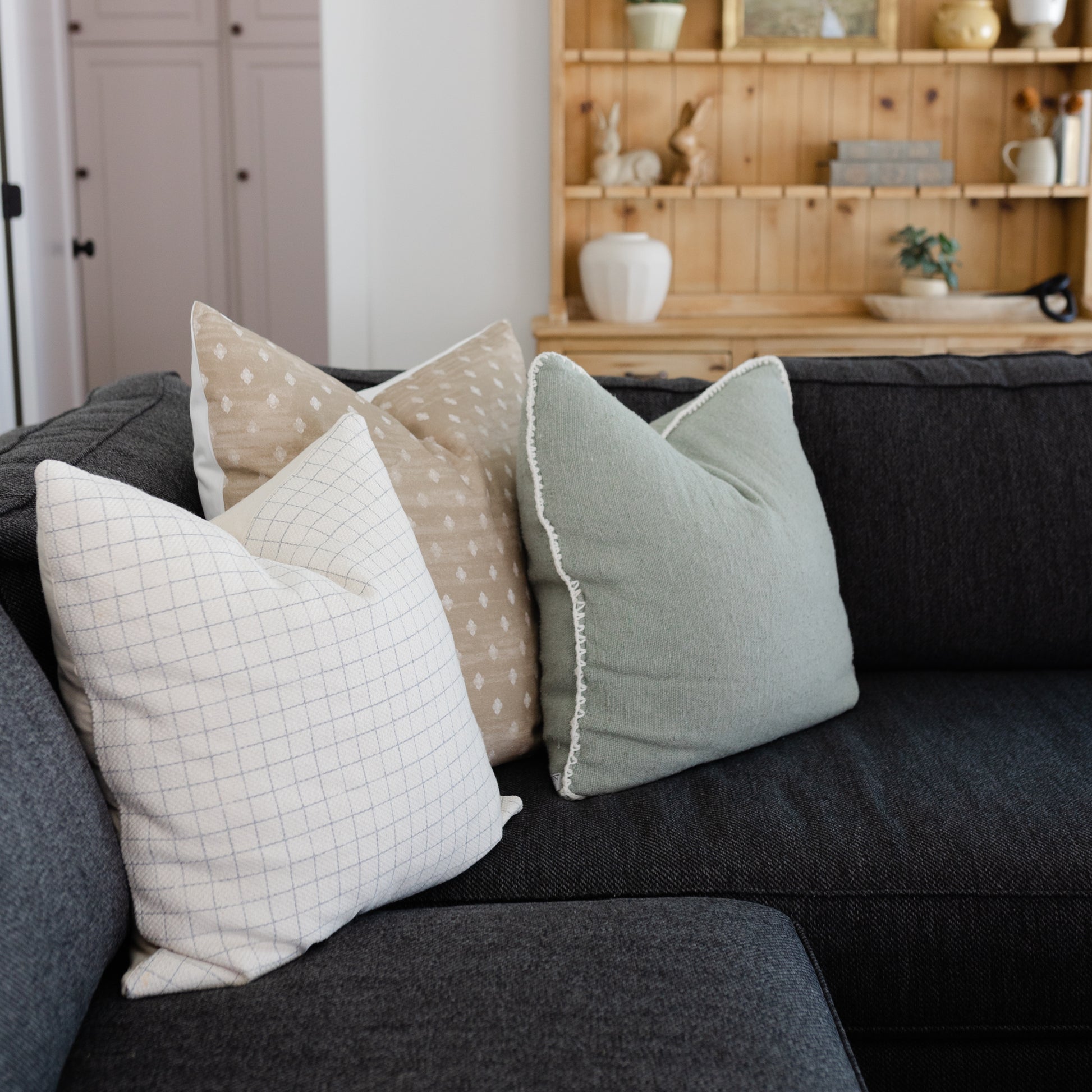 Three decorative pillows with grid and dot patterns in cream, tan, and sage green on a dark gray sofa.