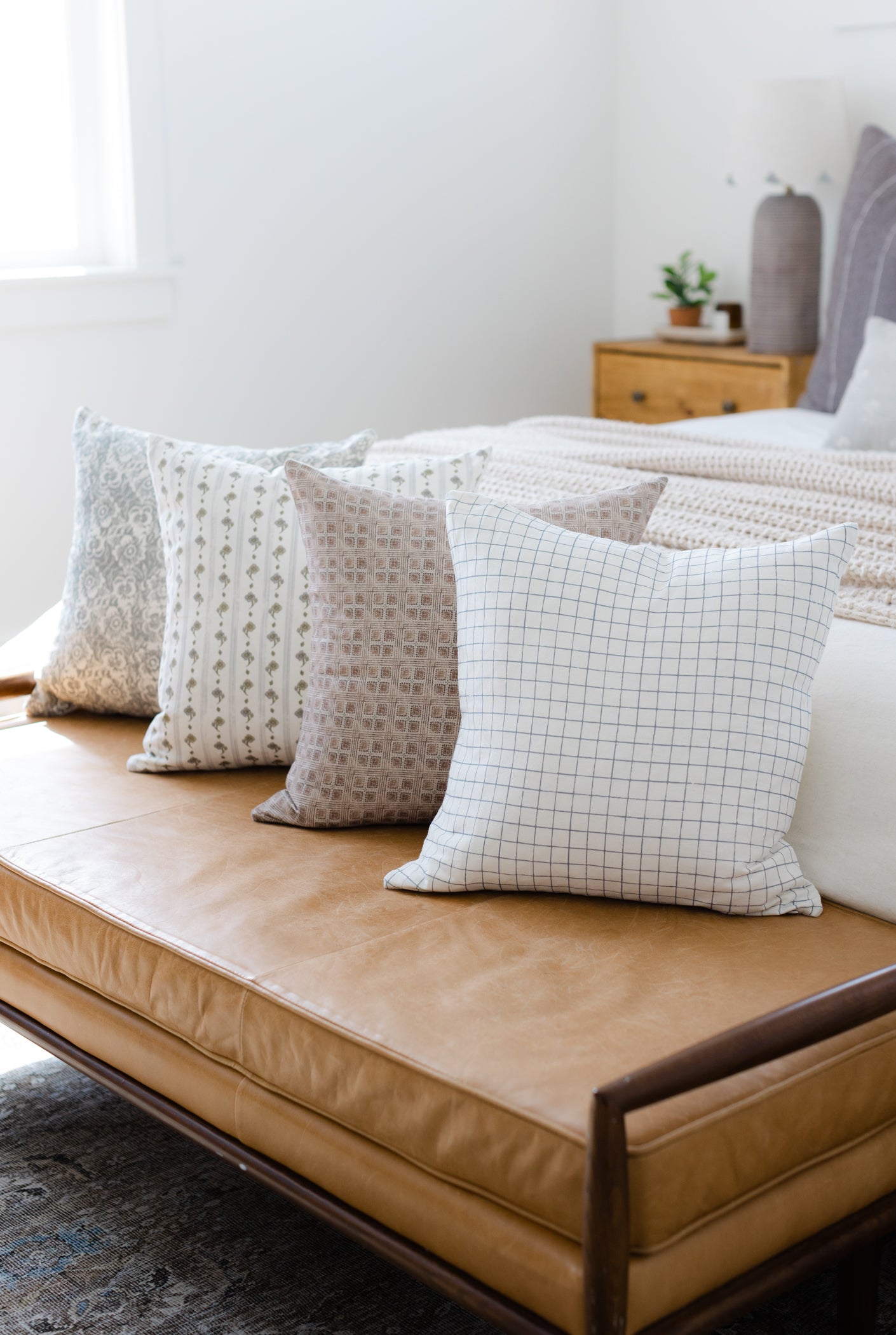Four decorative pillows in varied patterns: floral, dotted stripe, textured grid, and grid check in neutral tones arranged on