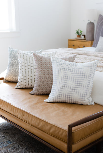 Four decorative pillows in varied patterns: floral, dotted stripe, textured grid, and grid check in neutral tones arranged on