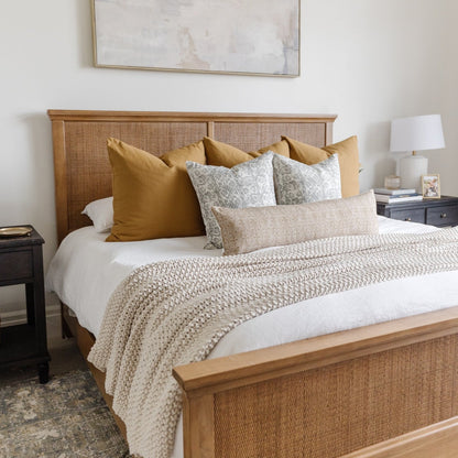 Floral patterned throw pillow in cream and sage green displayed on a bed with gold and neutral bedding.