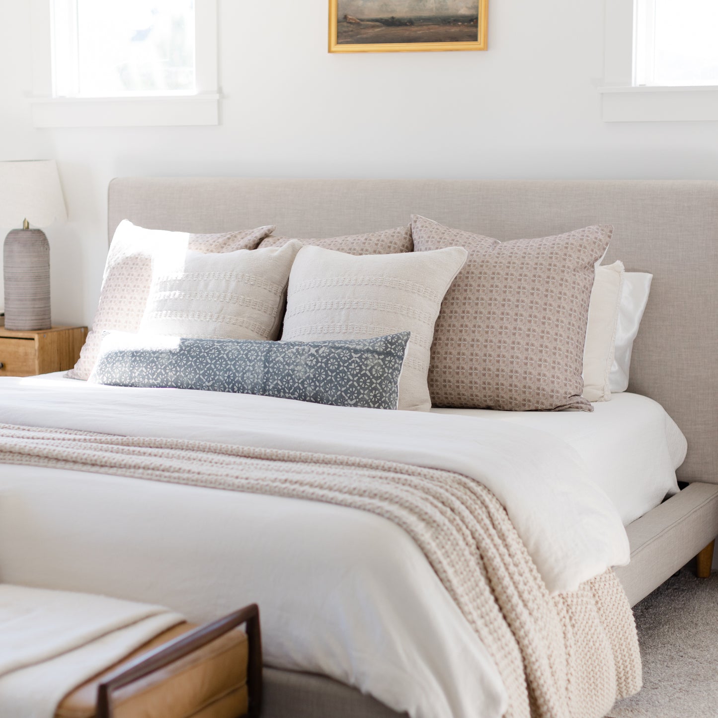Brown grid patterned euro pillow displayed among coordinating neutral pillows on a bed.