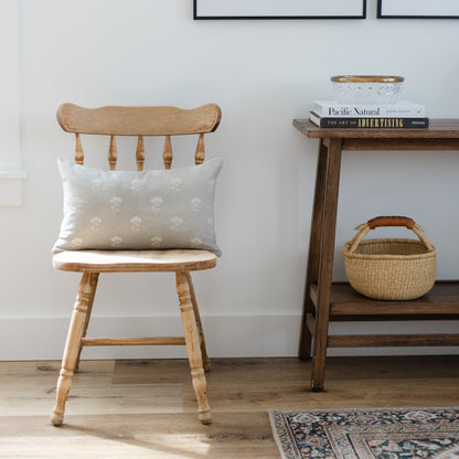 Gray lumbar pillow with floral pattern displayed on wooden chair.