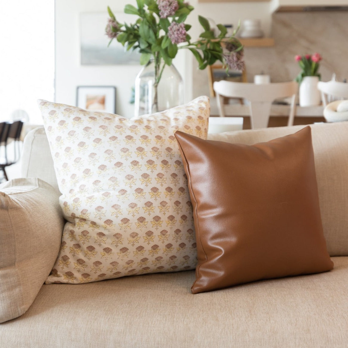 White floral patterned pillow with tan leaf print displayed on beige sofa.