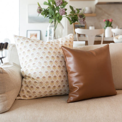 White floral patterned pillow with tan leaf print displayed on beige sofa.