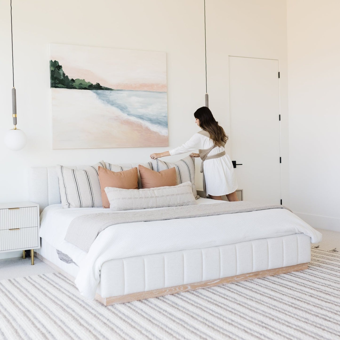 White upholstered bed with vertical channeling, displayed in a bedroom setting with coastal artwork and striped bedding.
