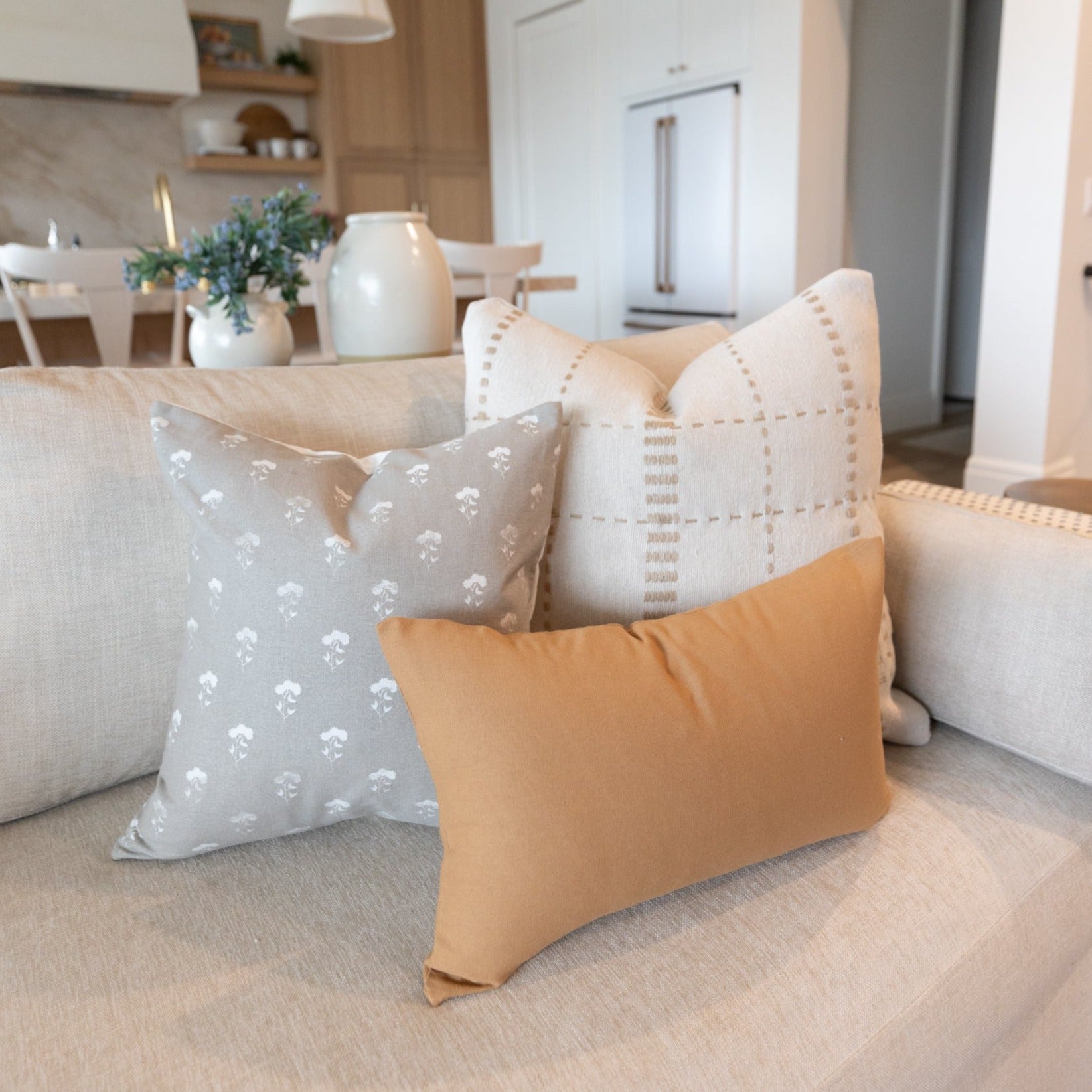 Gray pillow with white floral pattern displayed on beige sofa with coordinating pillows in neutral tones.