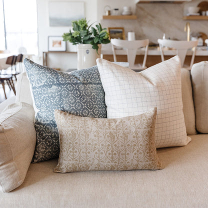 Three decorative pillows in blue, cream, and beige patterns arranged on a light-colored sofa.