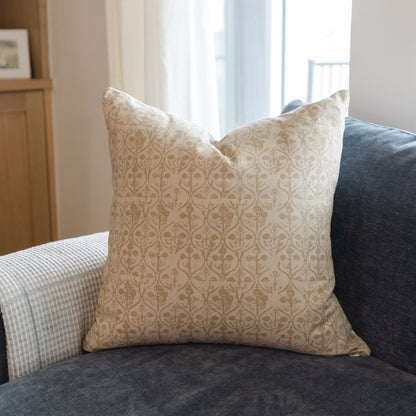 Cream-colored pillow cover with tan hourglass-shaped floral damask pattern displayed on a sofa.