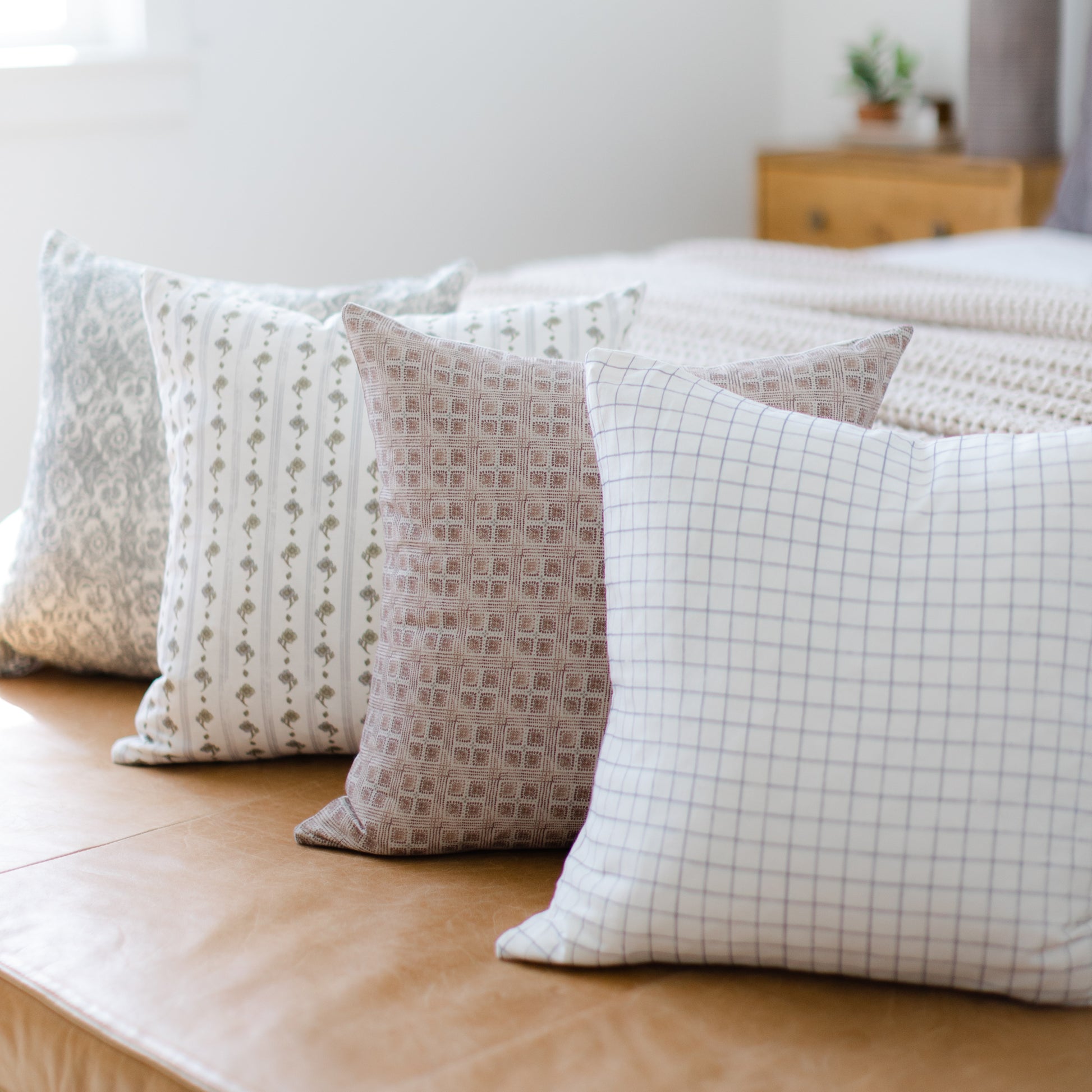 Four decorative pillows in varying neutral patterns including geometric and grid designs, arranged on a wooden floor.