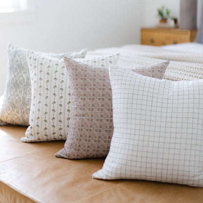 Four decorative pillows in varying neutral patterns including geometric and grid designs, arranged on a wooden floor.