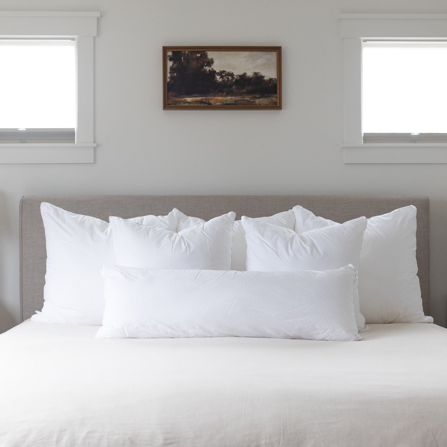 King bed set with white pillows and sheets arranged on gray upholstered headboard.
