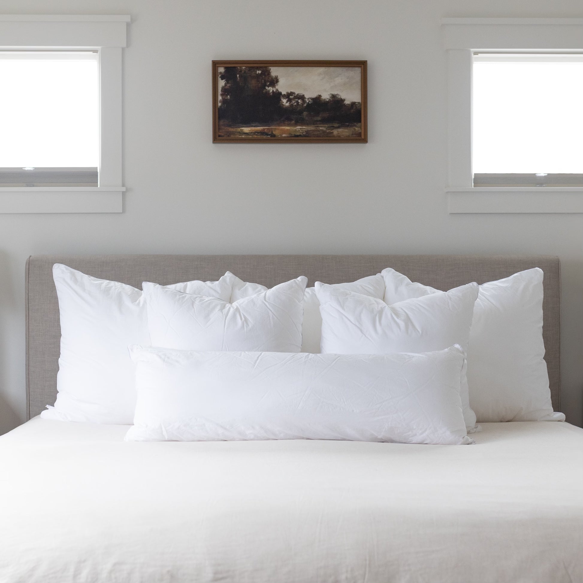 King bed set with white pillows and sheets arranged on gray upholstered headboard.