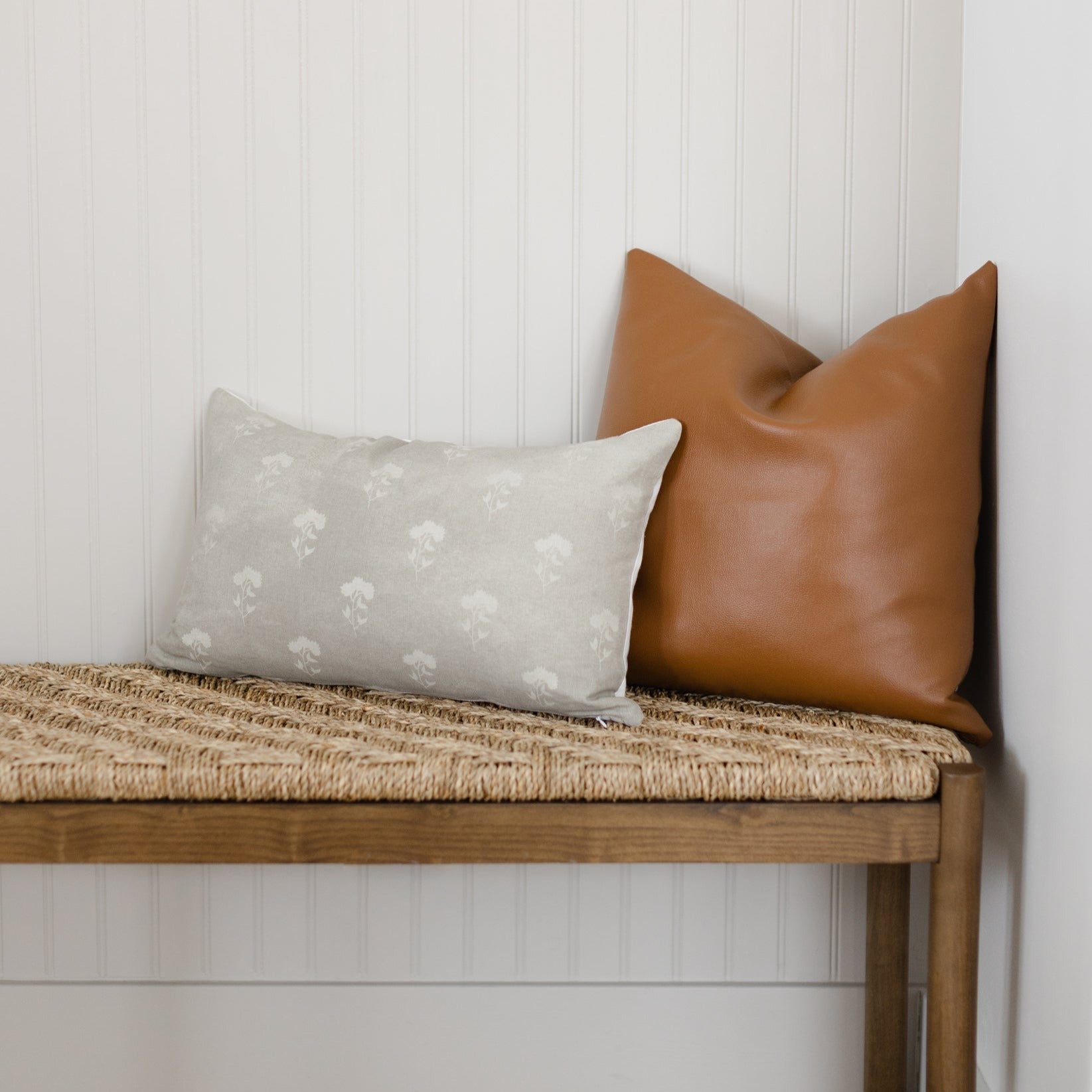 Gray lumbar pillow with white floral pattern displayed on wooden bench.