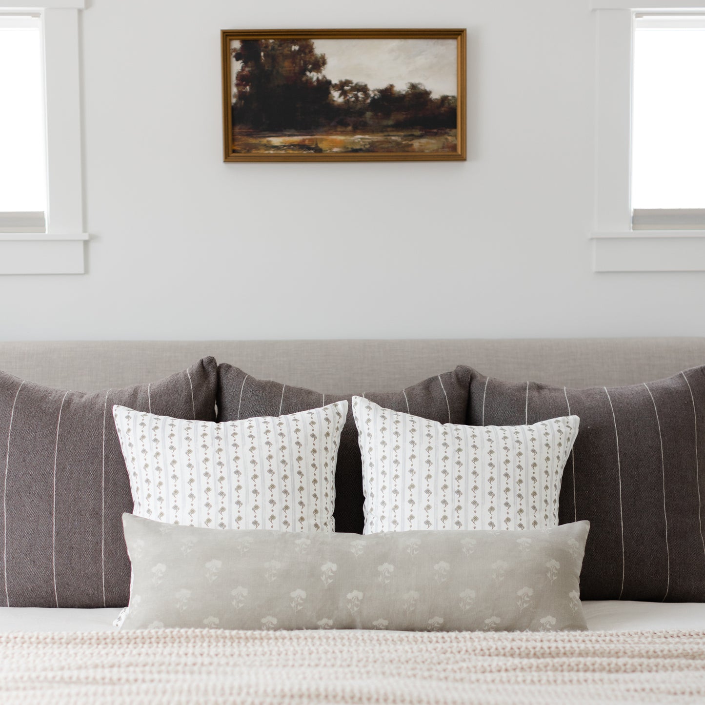 Gray lumbar pillow with small-scale floral pattern displayed on bed with matching decorative pillows.