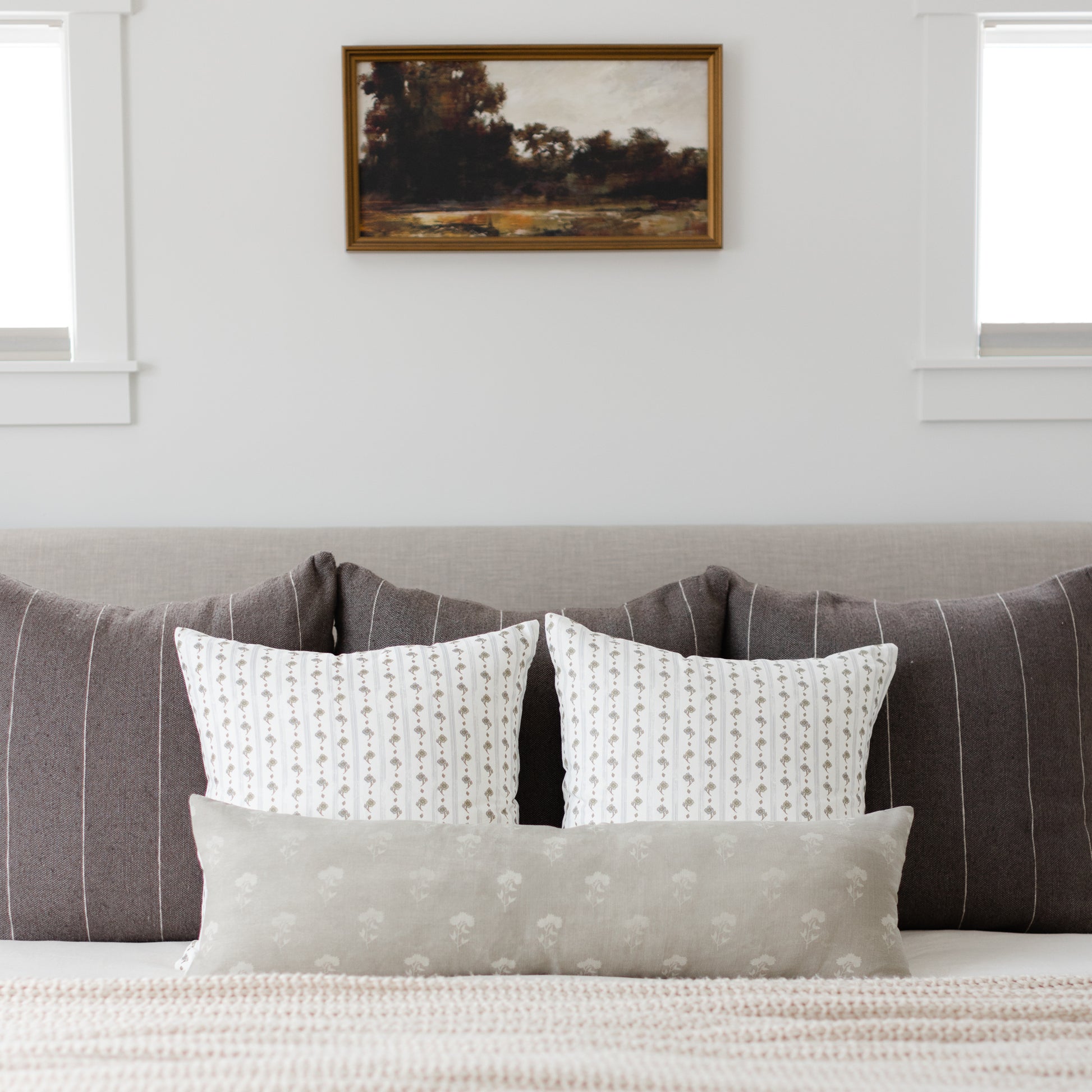 Gray lumbar pillow with small-scale floral pattern displayed on bed with matching decorative pillows.