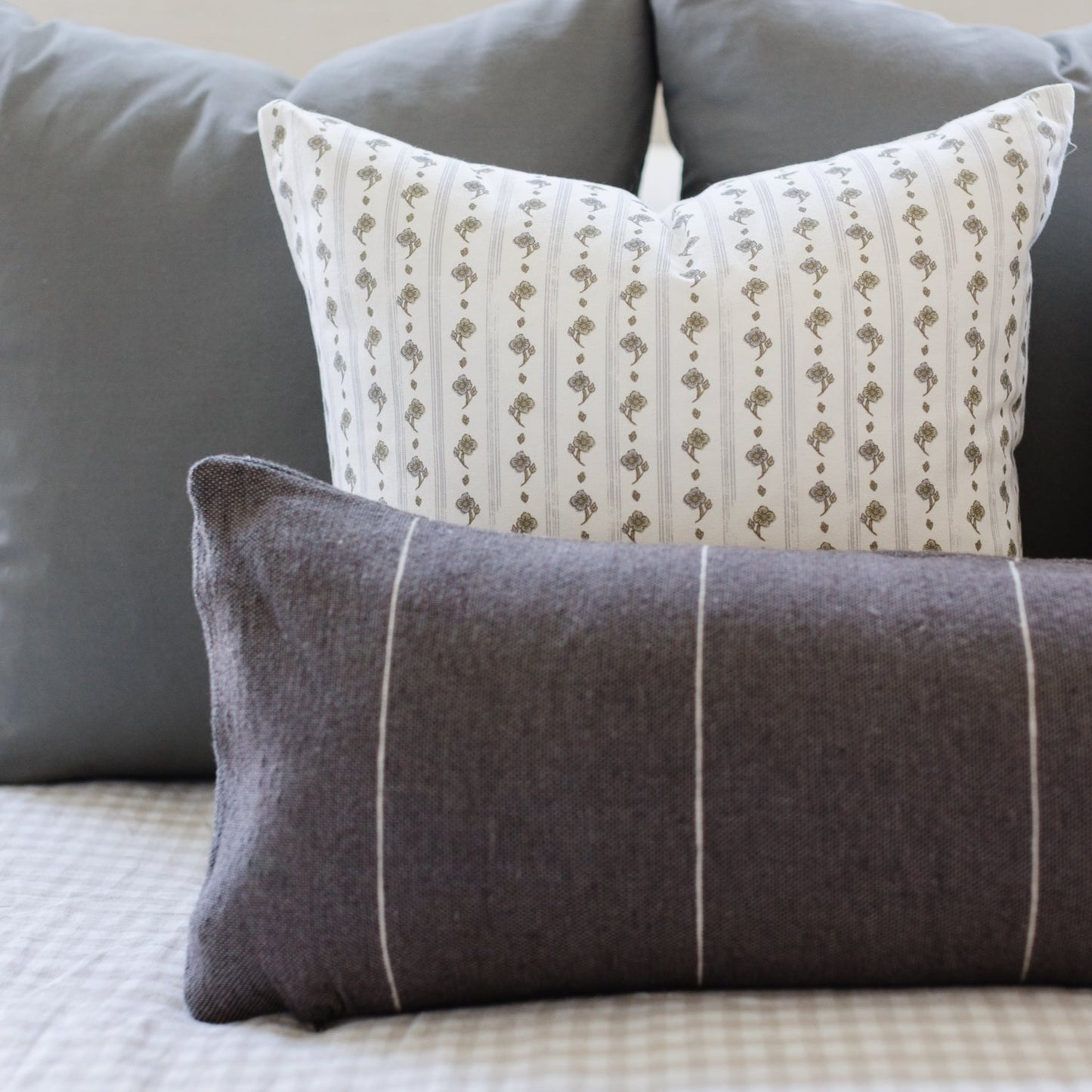 Cream pillow with vertical green floral stripes and small geometric patterns, displayed with gray striped pillow on gray sofa