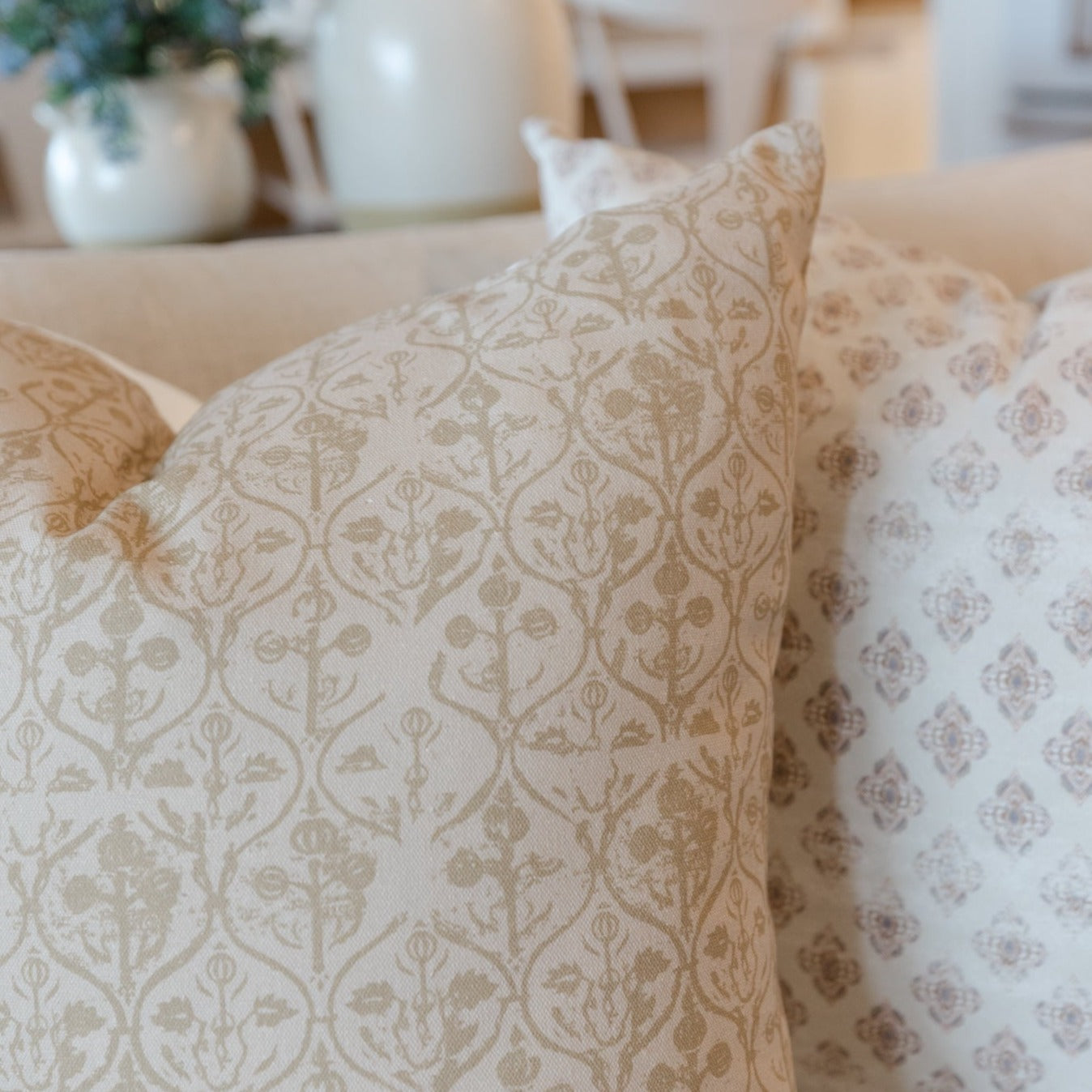 Beige and cream pillow cover with hourglass-shaped floral damask pattern displayed on sofa.