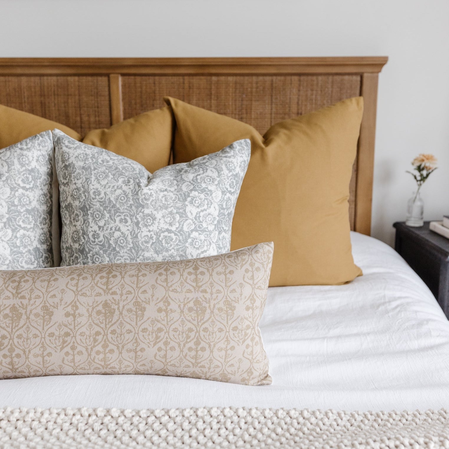 Decorative pillows on bed with gray floral, gold solid, and beige damask patterns arranged against wooden headboard.