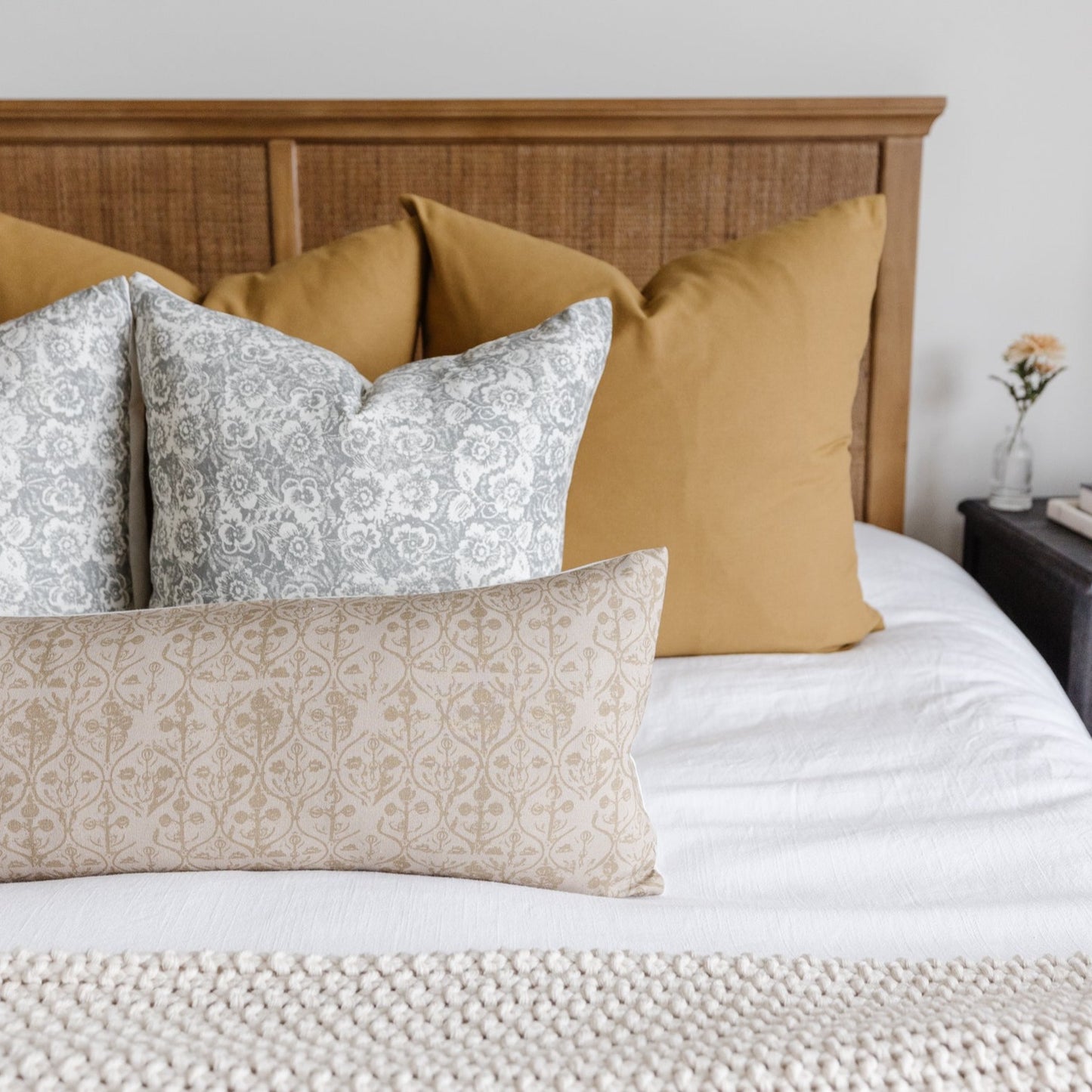 Decorative pillows with gray and beige floral damask patterns arranged on a bed with mustard and neutral solid pillows.