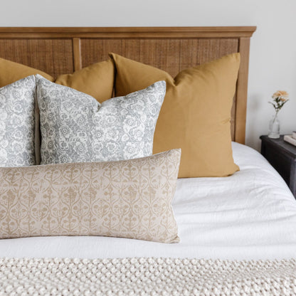Decorative pillows with gray and beige floral damask patterns arranged on a bed with mustard and neutral solid pillows.