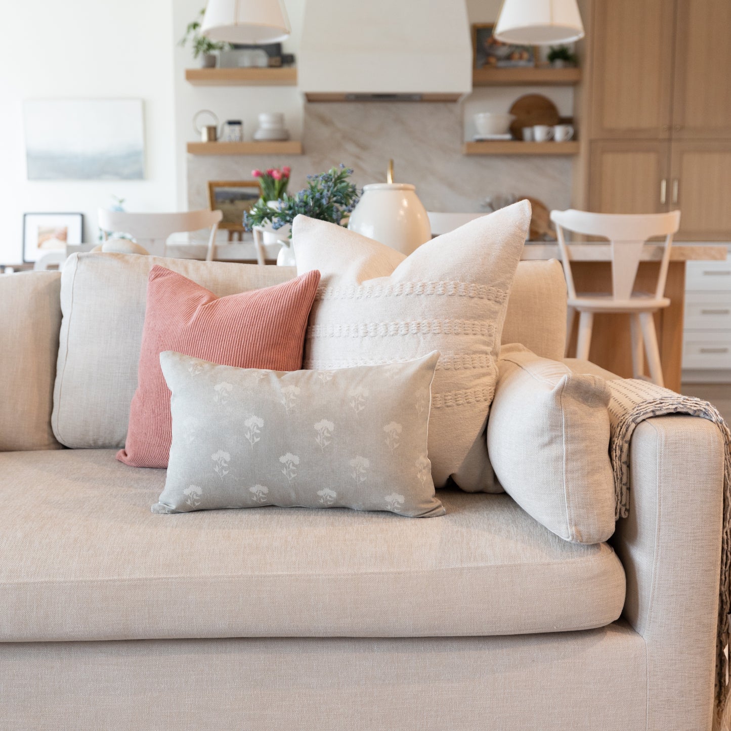 Gray lumbar pillow with small white floral pattern displayed among neutral throw pillows on a beige sofa.