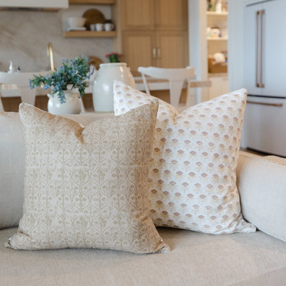 Two white and tan floral patterned throw pillows displayed on a light beige sofa in a kitchen setting.