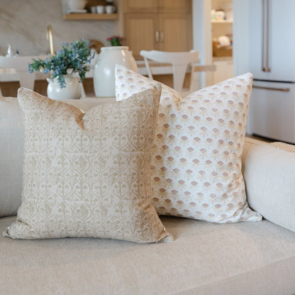 Two square pillow covers with tan and cream floral patterns displayed on a beige sofa.