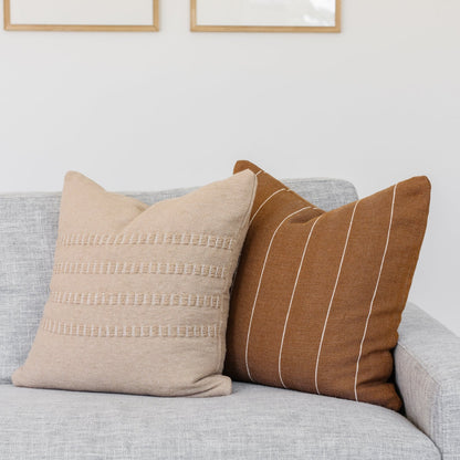 Tan and cream textured throw pillows with geometric patterns displayed on a gray sofa.