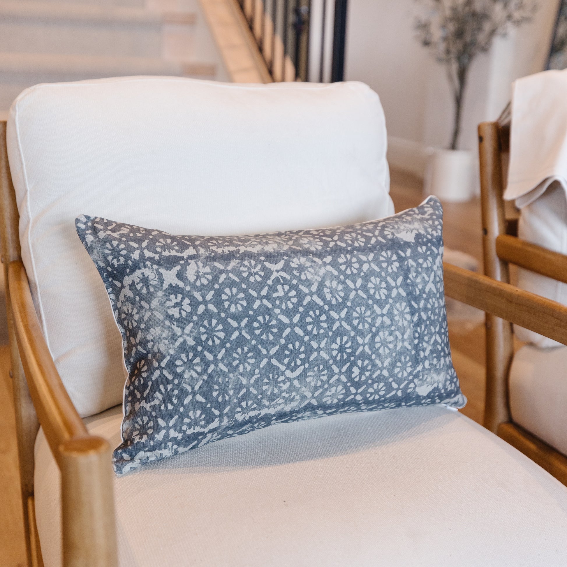 Blue-gray lumbar pillow with white diamond floral pattern on wooden chair.