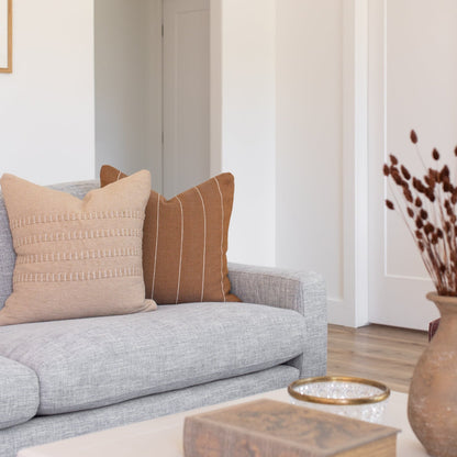 Tan throw pillow with geometric texture pattern displayed on gray upholstered sofa.