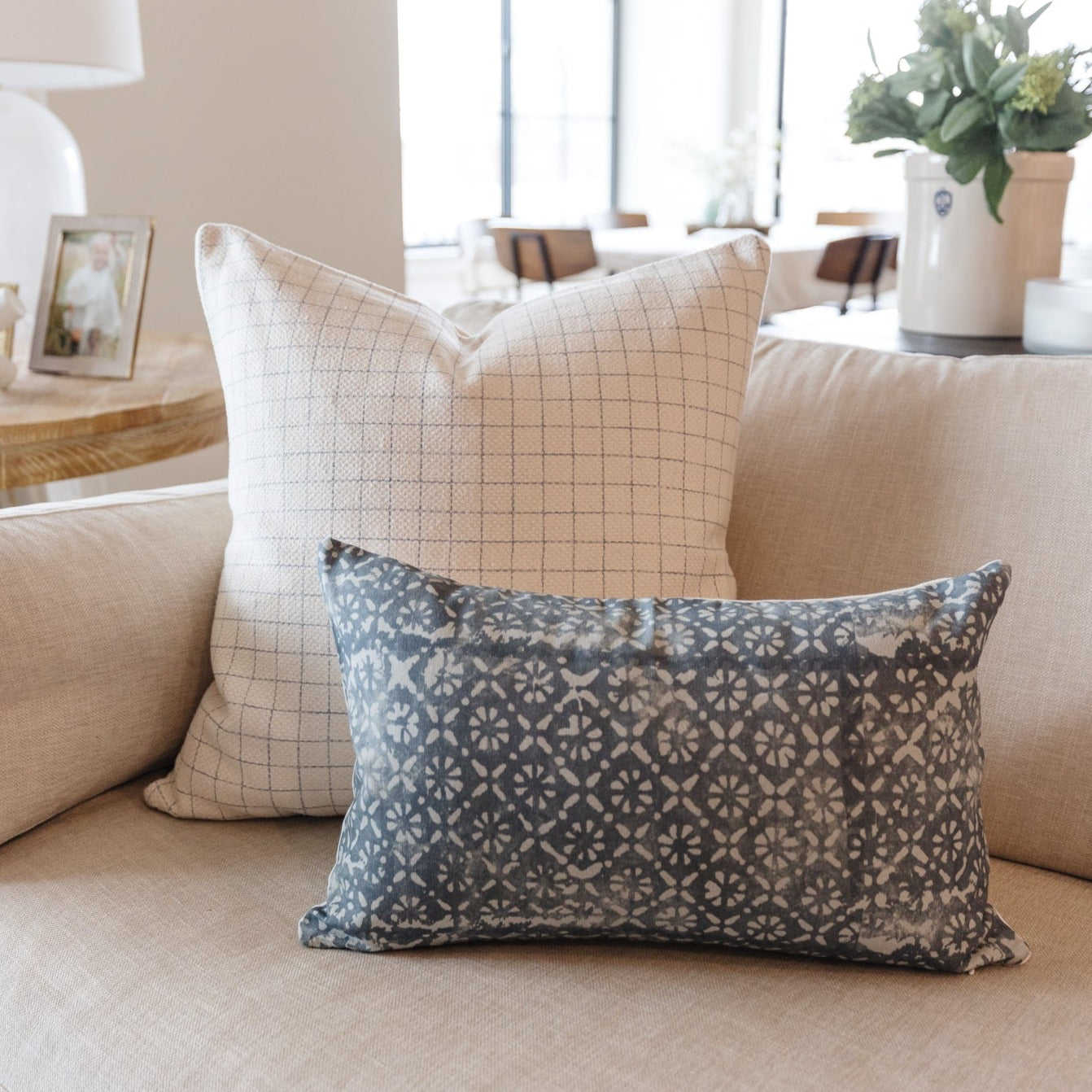 Lumbar pillow with blue geometric daisy pattern on beige textured sofa, displayed alongside grid-patterned square pillow.