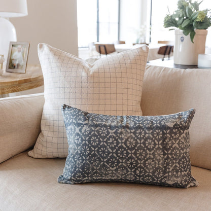 Lumbar pillow with blue geometric daisy pattern on beige textured sofa, displayed alongside grid-patterned square pillow.