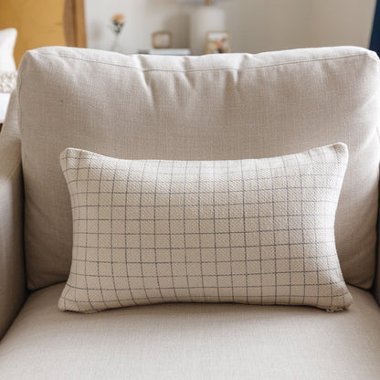 Rectangular lumbar pillow with tan grid pattern on cream linen, displayed on beige chair.