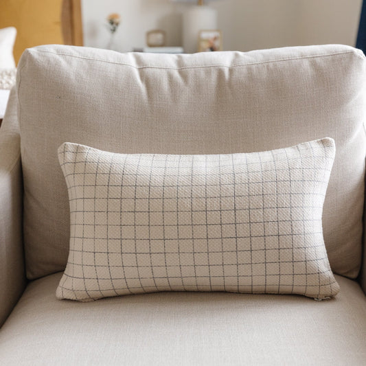 Rectangular lumbar pillow with tan grid pattern on cream linen, displayed on beige chair.