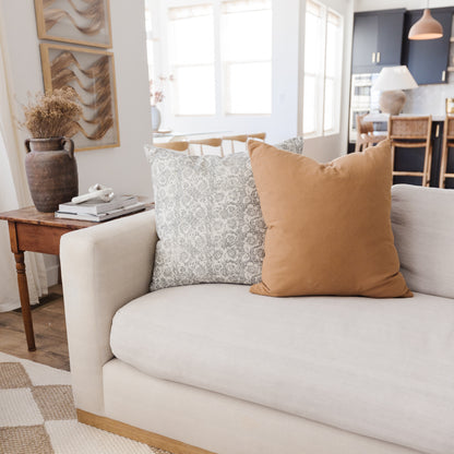 Terracotta-colored and patterned throw pillows displayed on a cream sofa in a living room setting.