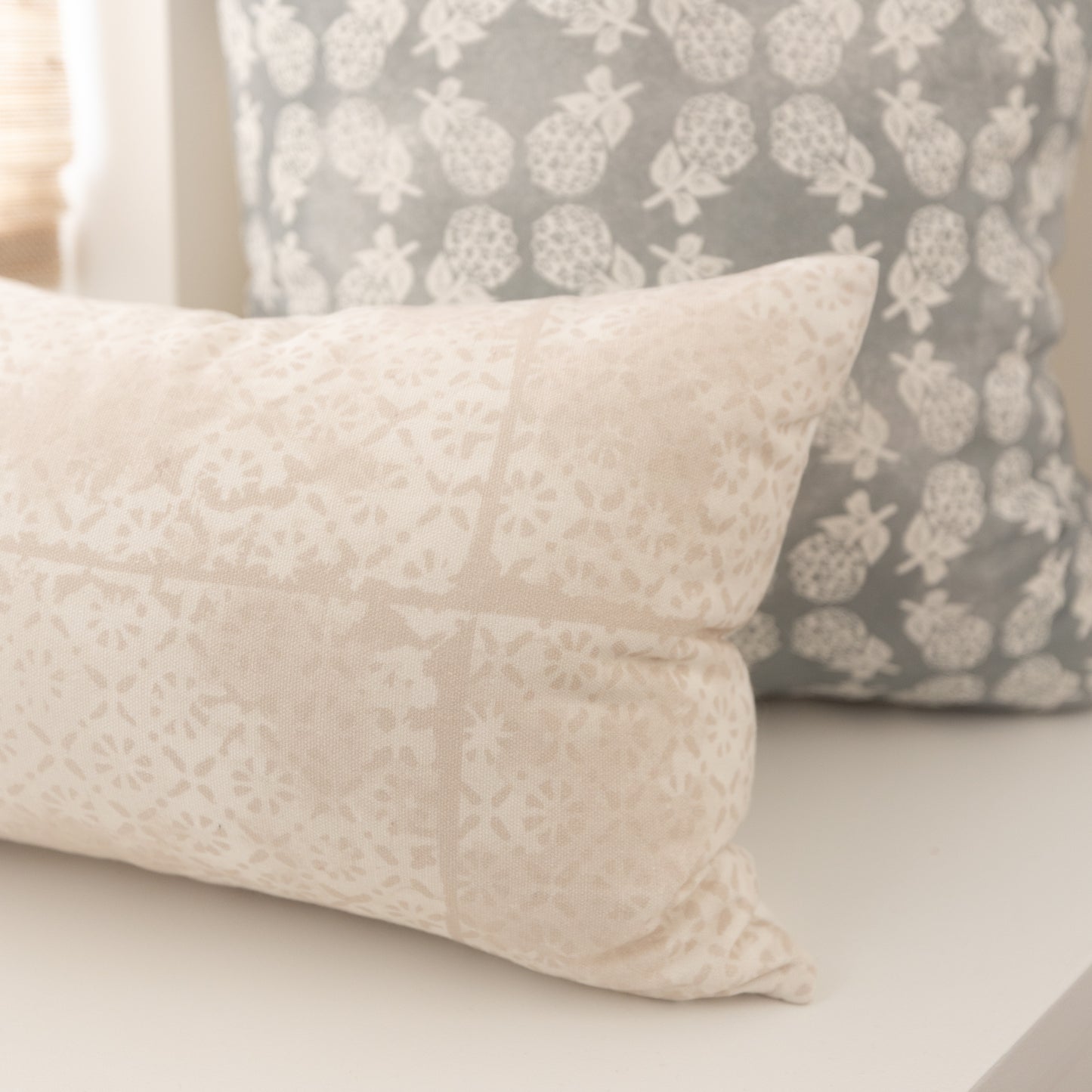 Cream lumbar pillow with faded floral pattern displayed next to gray pillow with white botanical print.